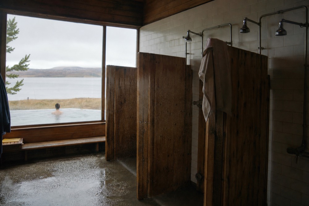 A row of wooden shower stalls along a tiled wall in a geothermal spa changing area