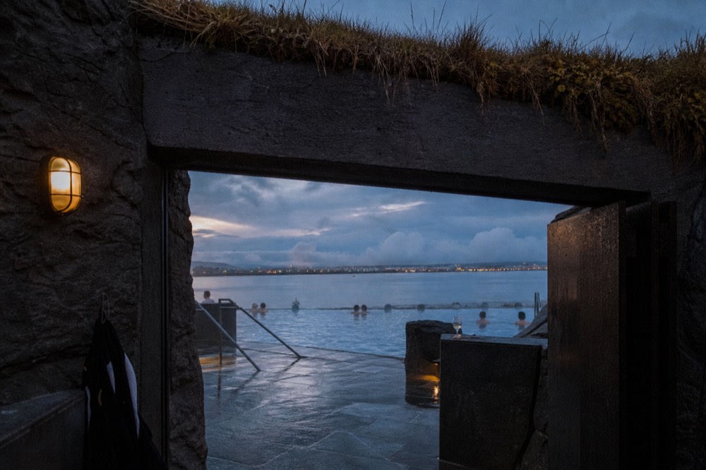 An evening view of a steaming infinity pool at dusk with city lights glowing in the distance