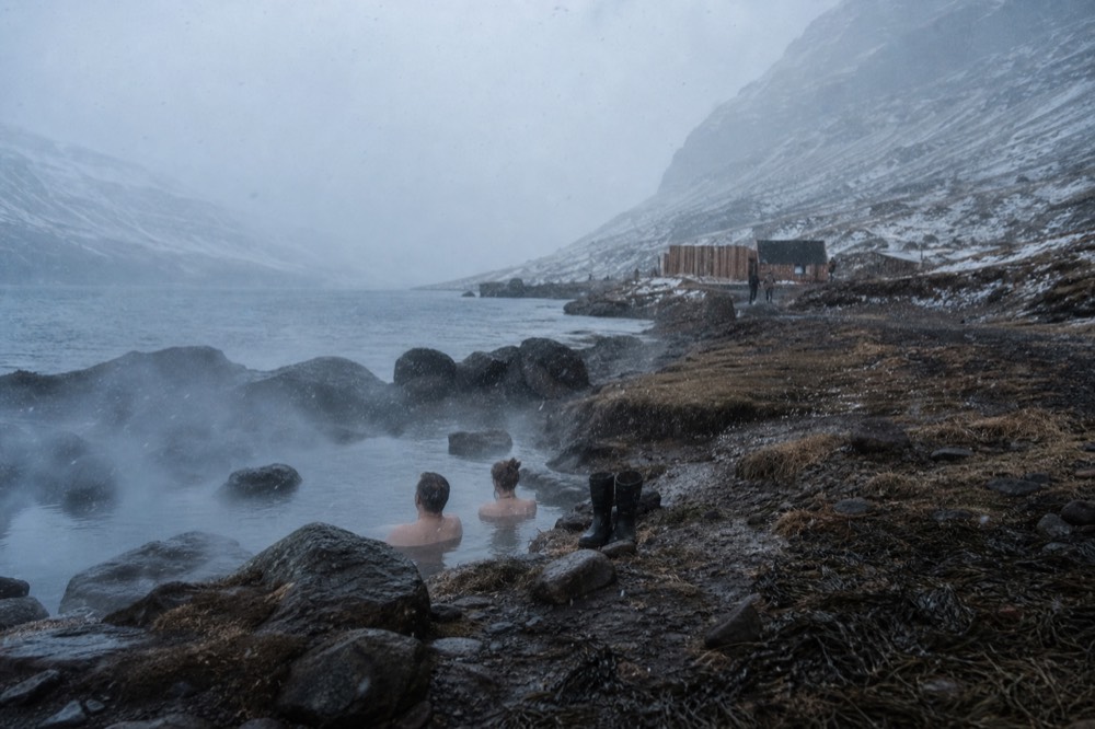 Natural hot spring pools on a dark fjord shoreline with hills behind
