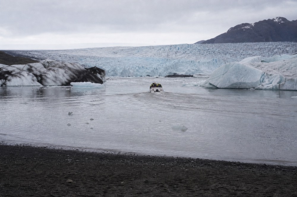 A small boat moving between icebergs on a glacial lagoon near a glacier wall
