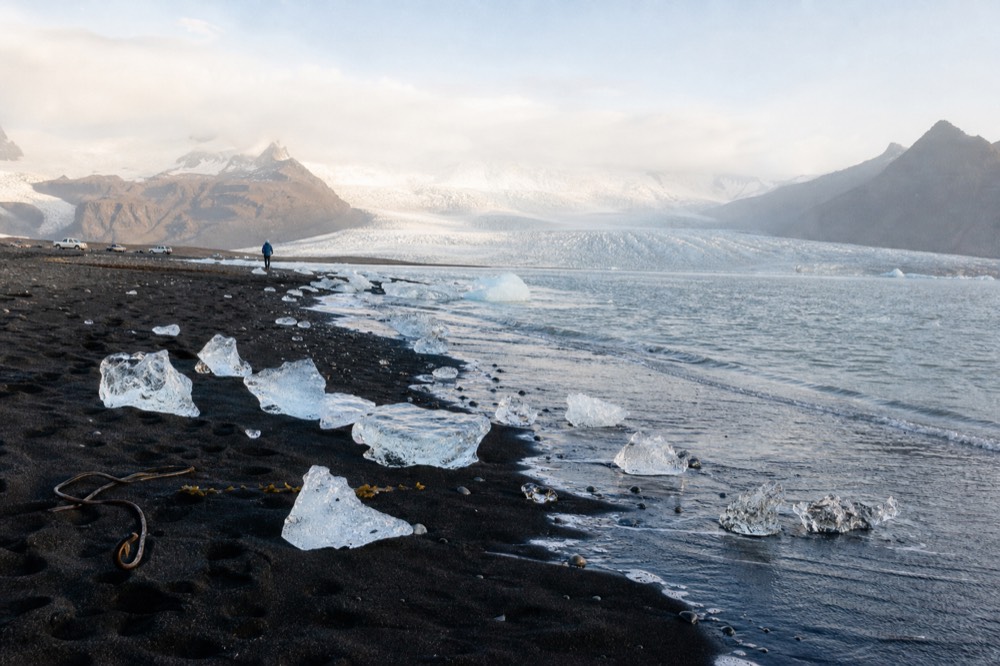 Chunks of clear ice resting on black volcanic sand at the edge of the sea