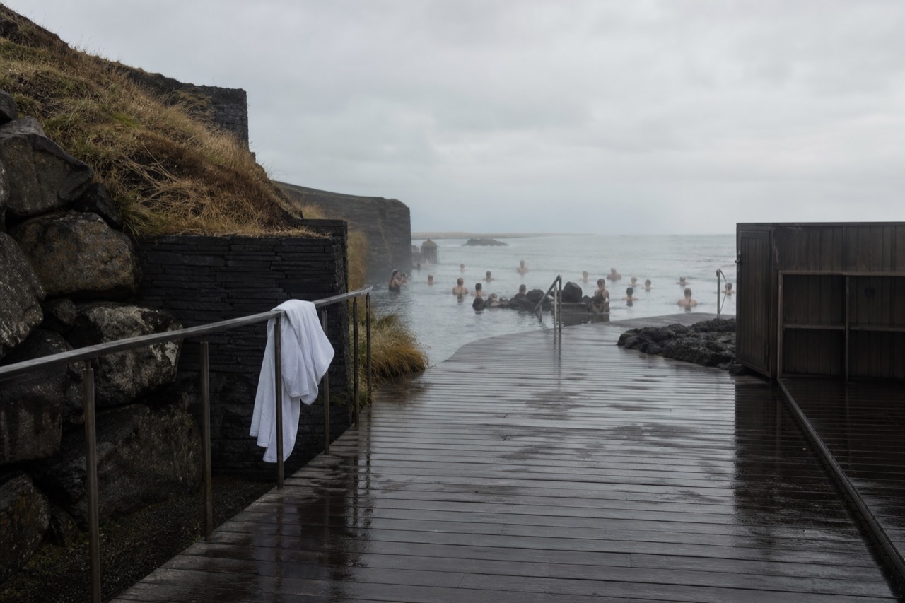 A wooden deck beside a steaming geothermal lagoon at the ocean's edge