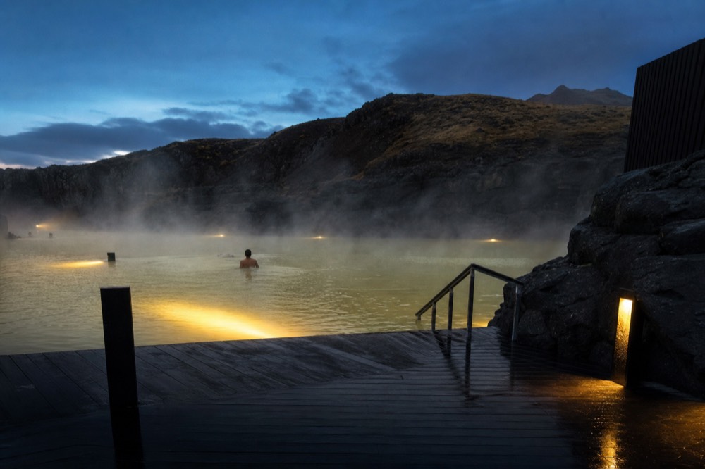 A geothermal pool at dusk with warm light on the water and dark hills beyond