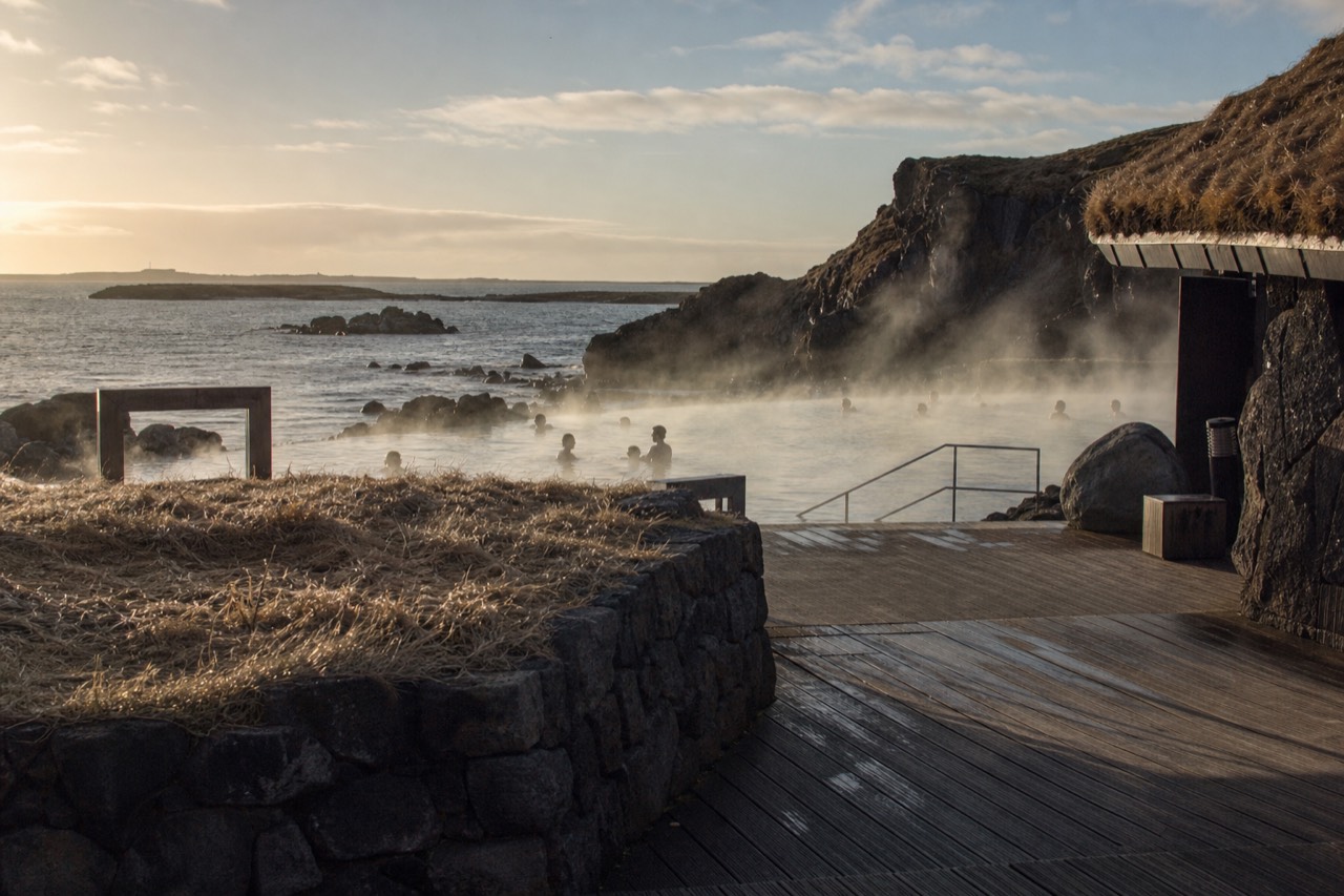 Steam rising from a geothermal lagoon at the edge of a dark lava coastline