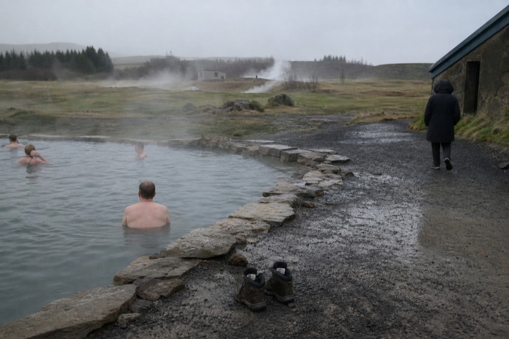 A steaming natural hot pool edged with rocks beside a gravel path in rural south Iceland