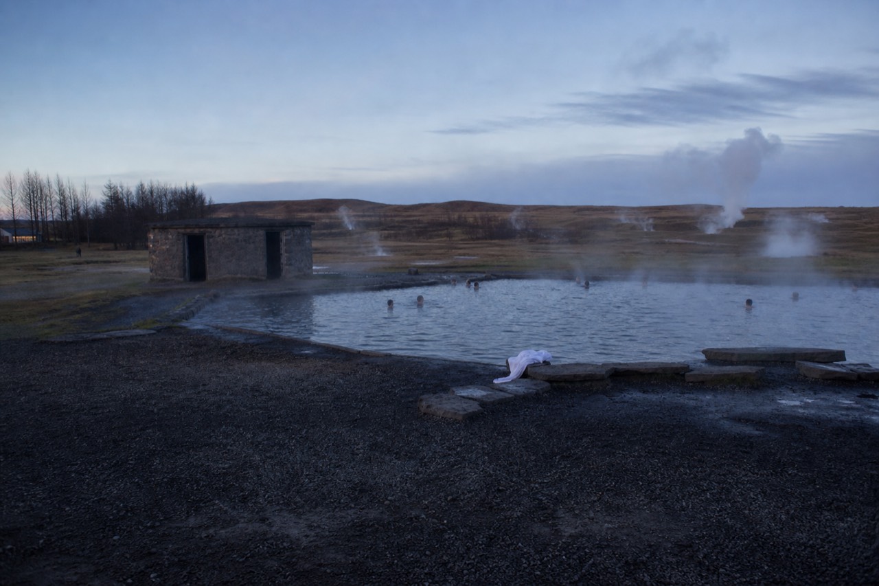Steaming geothermal pool surrounded by gravel and small vents at dusk in a rural Icelandic field