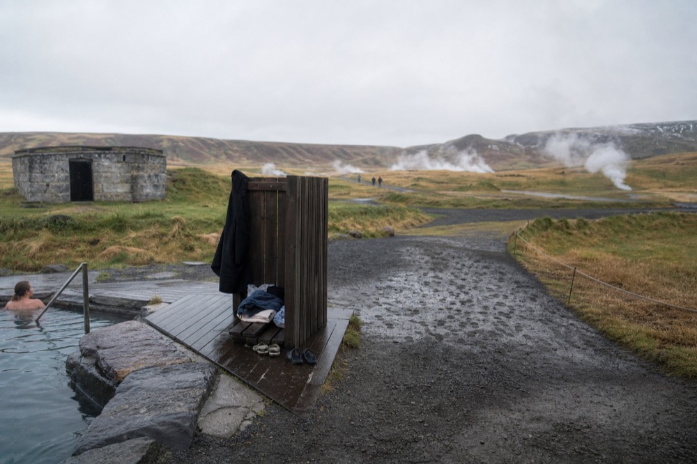 Small geothermal pool steaming beside a simple wooden deck in a rural setting