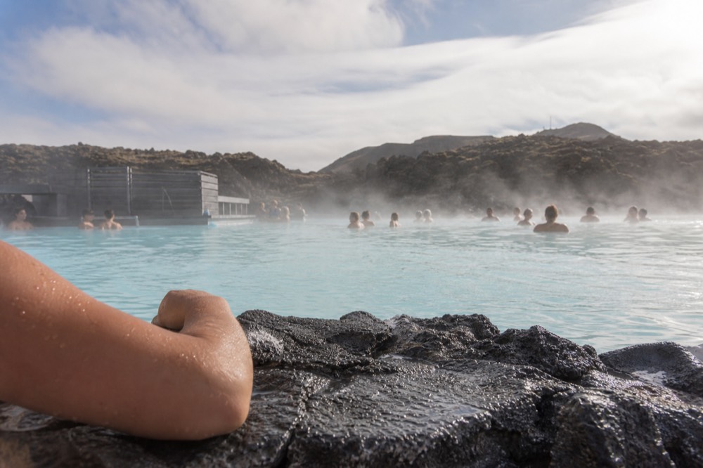 A swimmer's arm resting on the edge of a steaming blue lagoon