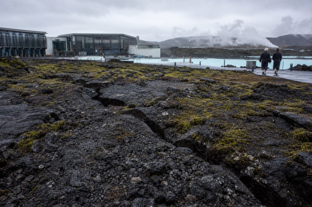 Steam rising from geothermal water against a landscape of cracked dark lava rock