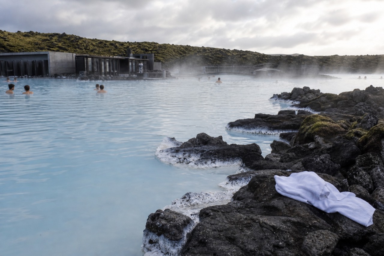 Steam rising from a pale blue geothermal lagoon surrounded by dark lava rock under a wide sky