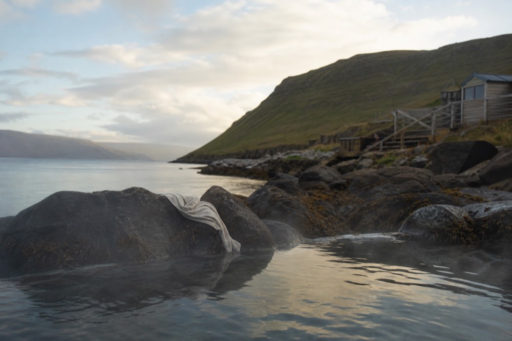 Steaming tidal pools at the edge of a calm fjord with low hills across the water
