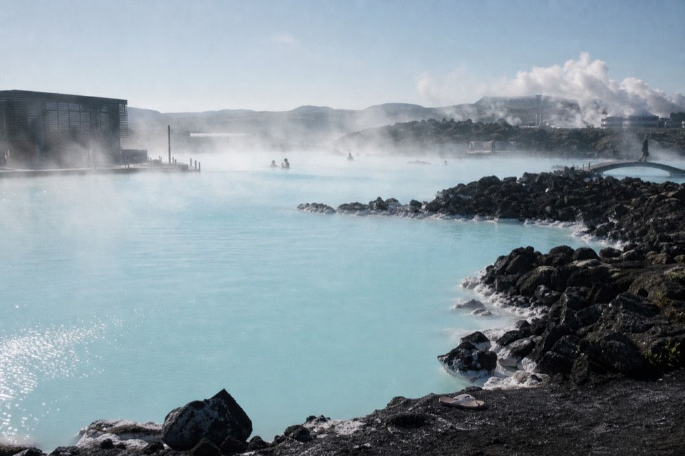 Steam drifting across a milky blue geothermal pool edged with dark volcanic rock