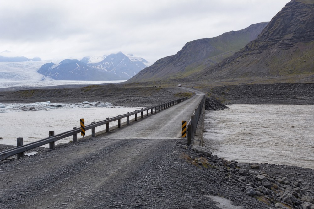 A single-lane bridge over a glacial river on an empty road in South Iceland