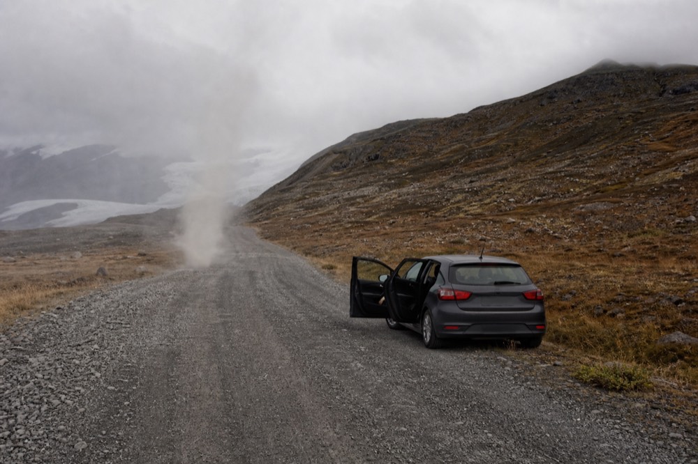 A gravel mountain road winding through bare brown hills under low cloud
