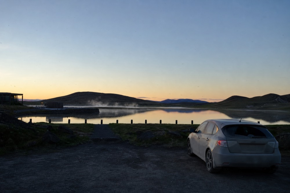 A calm lake at dusk with low hills and a band of clear sky above the water