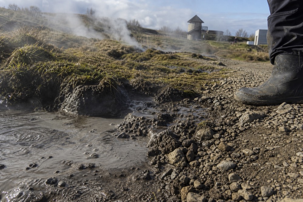 Small bubbling hot springs and steam vents beside a gravel path at a geothermal area