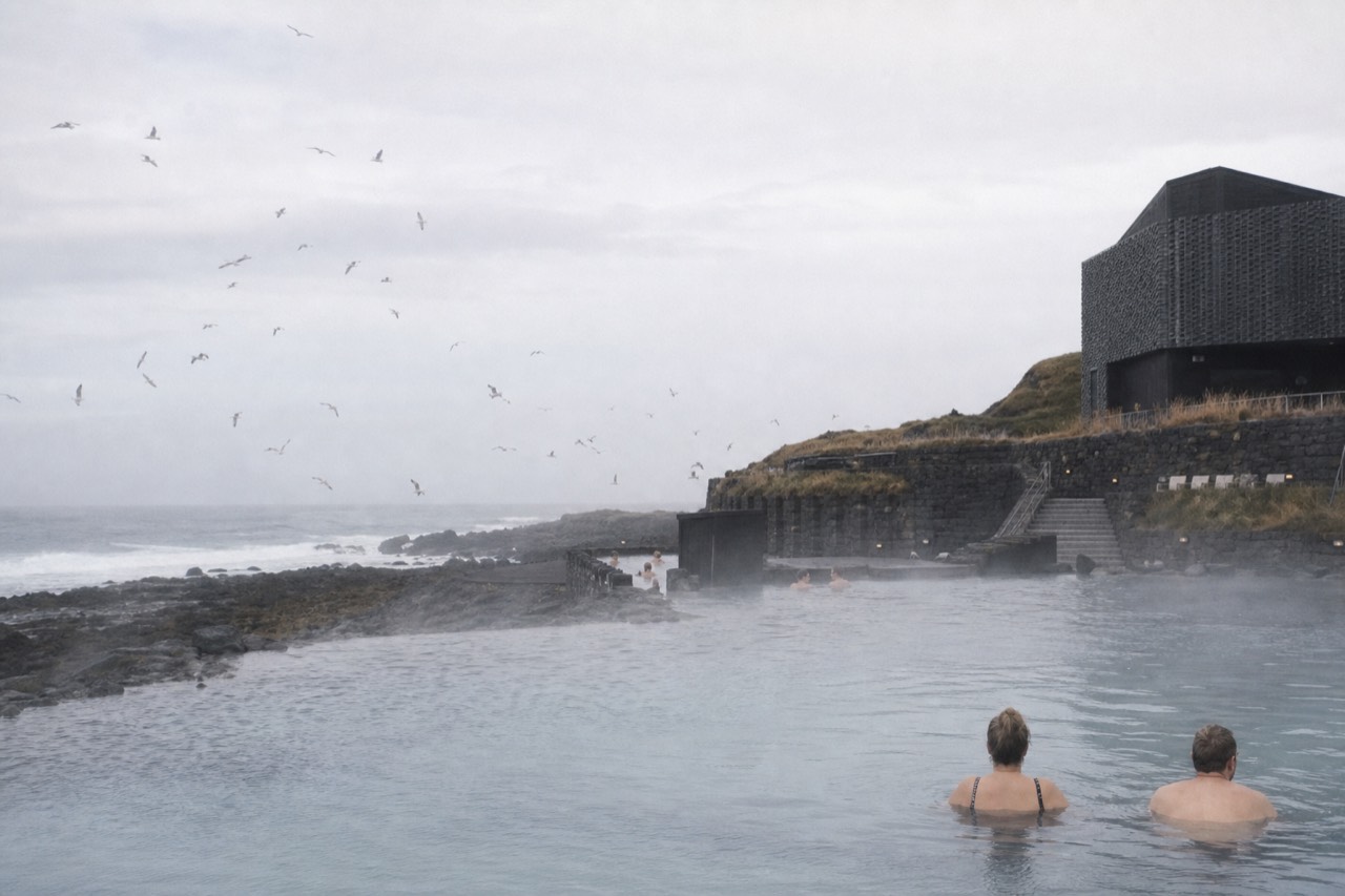 Steam rising from a geothermal lagoon at the edge of a dark lava shoreline in Iceland
