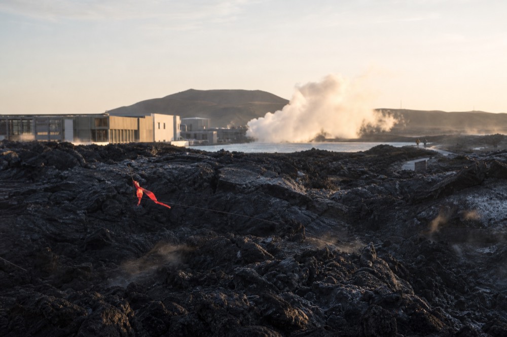 A volcanic fissure landscape with dark fresh lava rock stretching toward distant hills