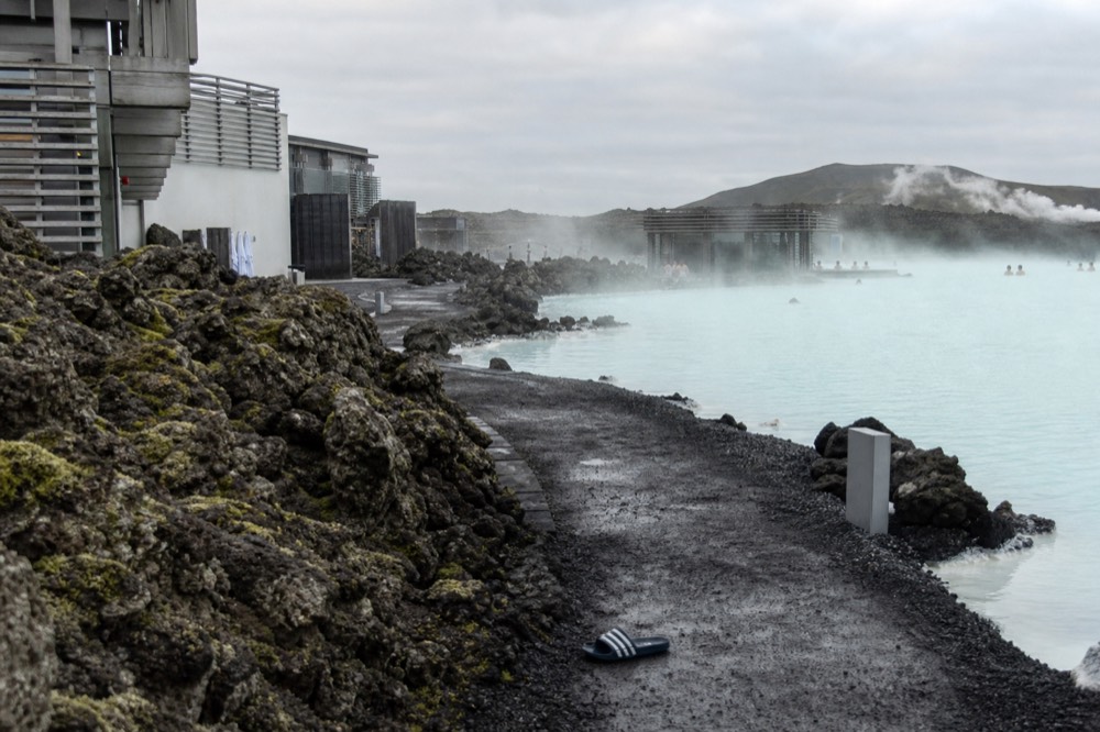 Pale turquoise geothermal water edged by dark volcanic rock with thin steam drifting across the surface