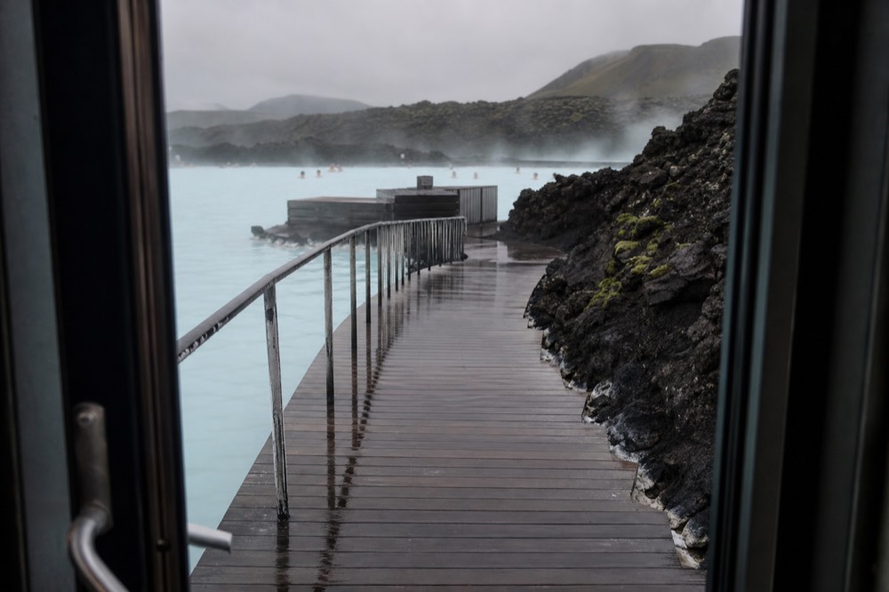 A wooden walkway curving between steaming blue pools on a dark lava field