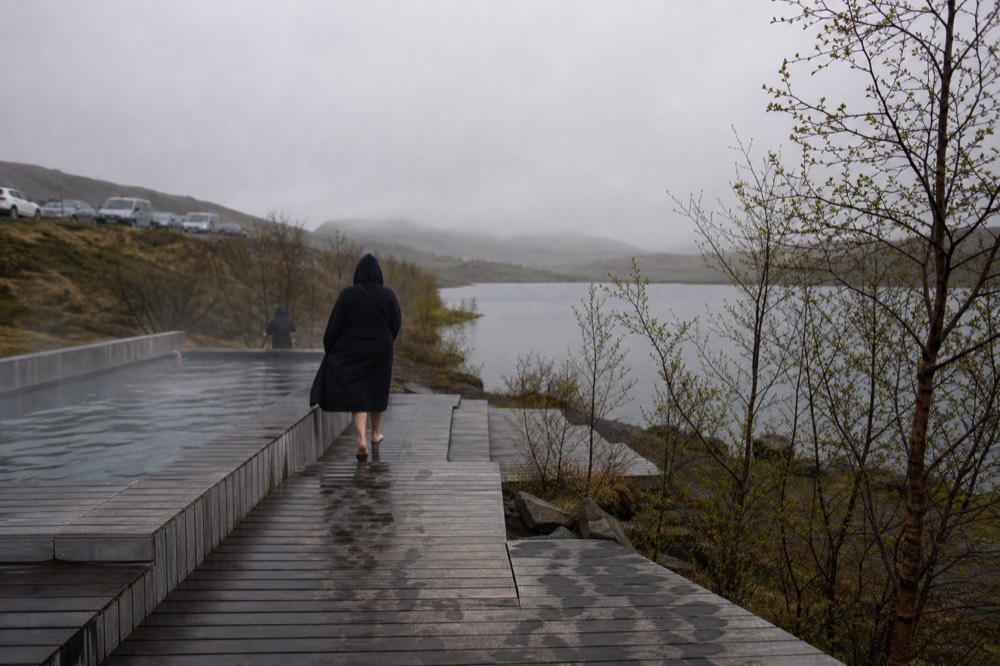 Steam rising from geothermal pools on the edge of a calm lake surrounded by low hills