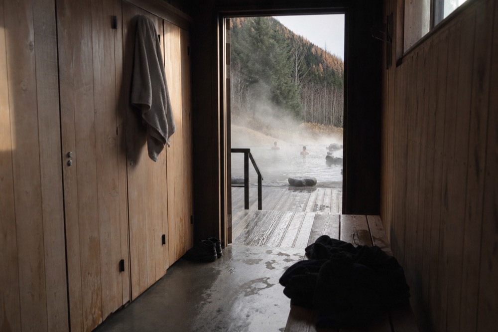 Communal changing room benches with wooden lockers beside a geothermal bathing area