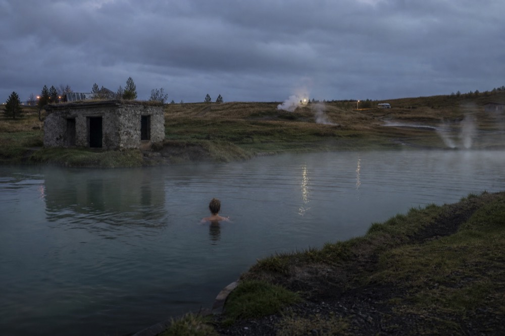 An outdoor geothermal pool at night with steam drifting across dark water