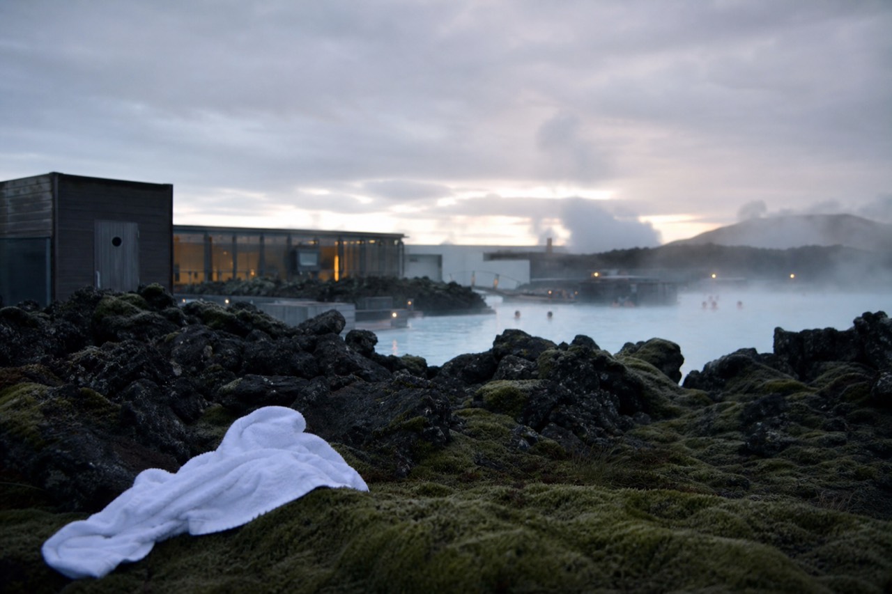 Steam rising from a geothermal lagoon beside dark volcanic rock at dusk