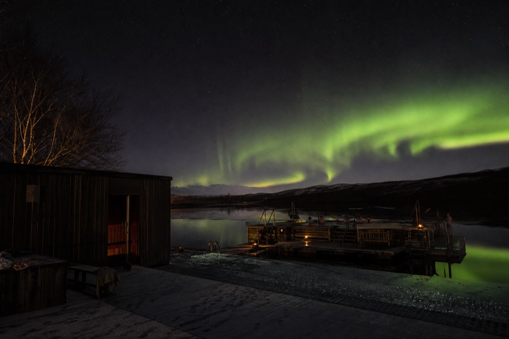 Green aurora ribbons over a still geothermal pool at night
