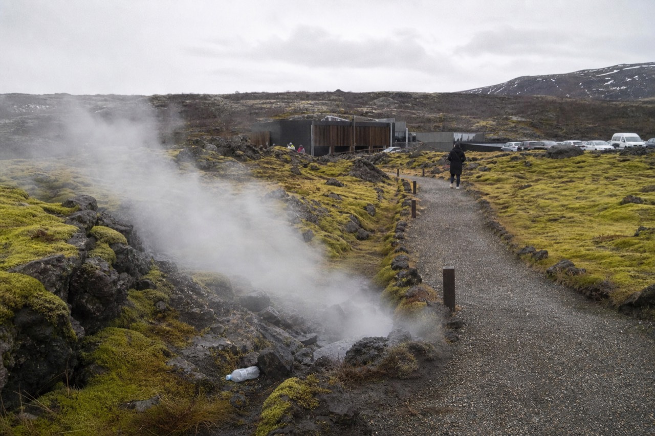 Steaming geothermal vents beside a gravel path in a mossy Icelandic lava field
