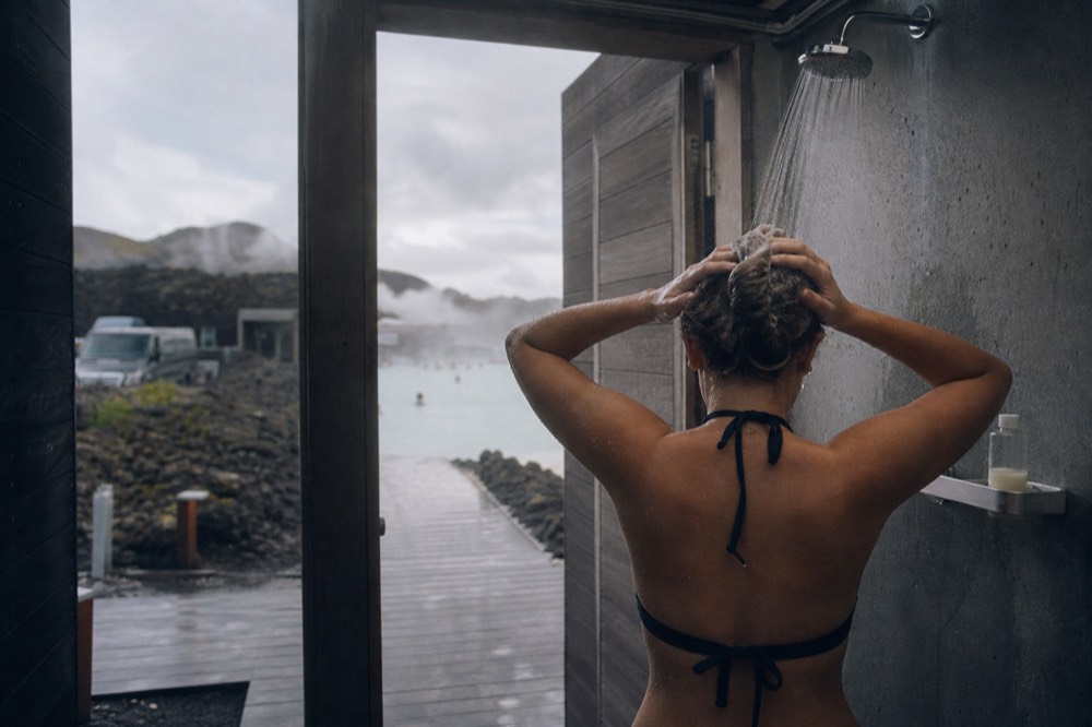 A visitor applying conditioner at a shower station before entering a steaming geothermal lagoon