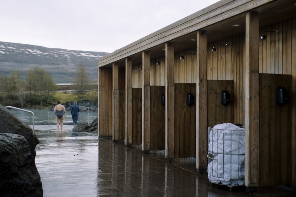 A row of shower cubicles with complimentary conditioner dispensers beside a geothermal spa entrance