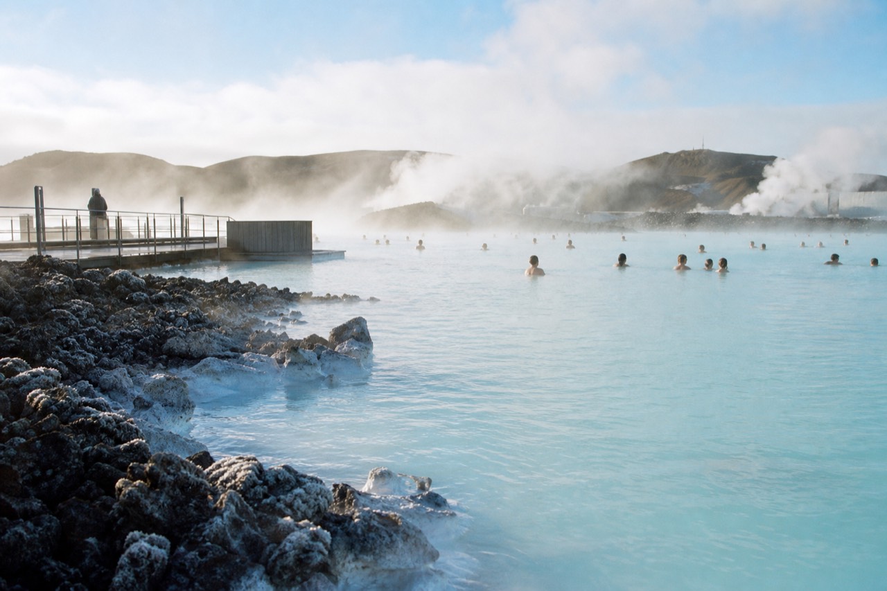 Steam rising from the pale blue water of a geothermal lagoon surrounded by dark lava rock