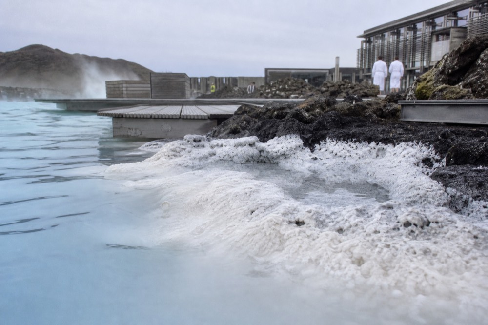 White silica deposits lining the edge of milky blue water on black lava