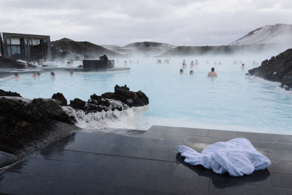 Steam drifting across warm blue water beside a slate terrace