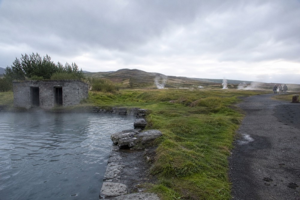 A still natural hot pool with steam rising beside a grassy bank