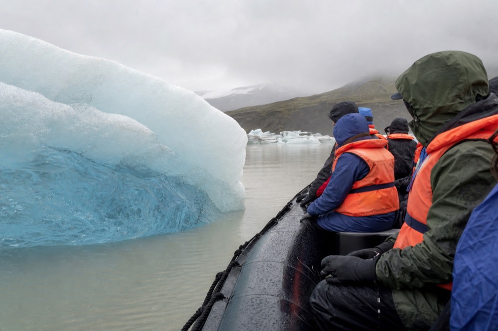 Passengers in life vests seated low in a Zodiac beside a rounded blue iceberg