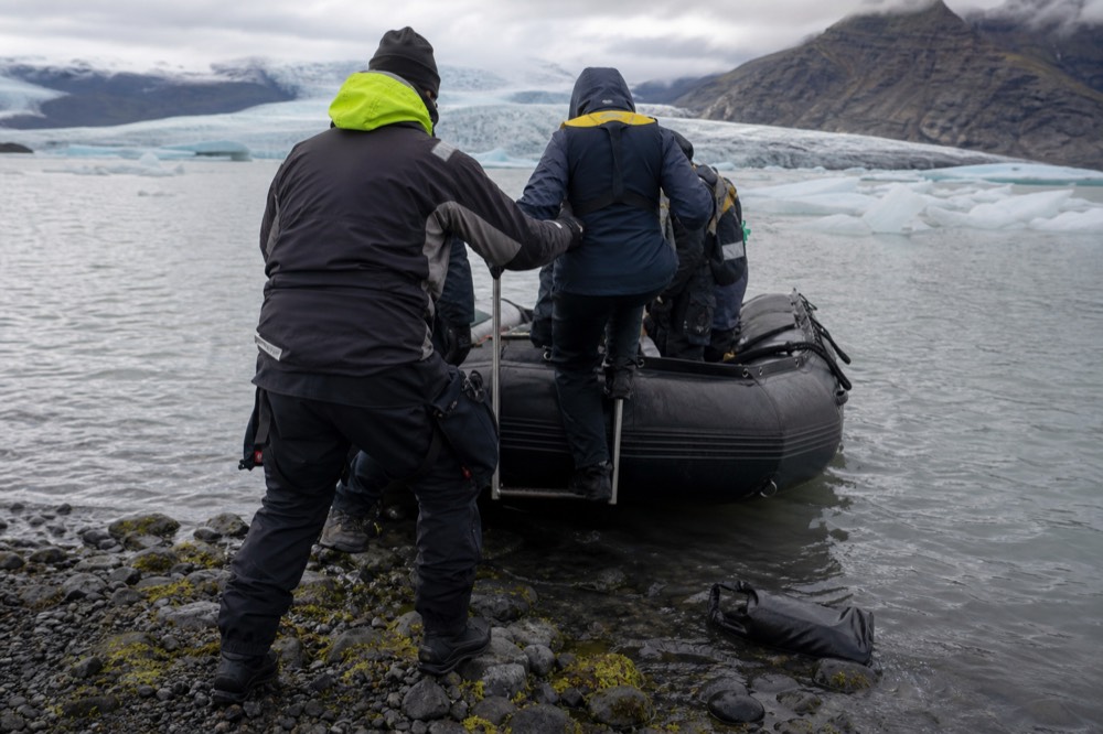 Guide in a drysuit helping a passenger from a Zodiac onto a rocky lagoon shore