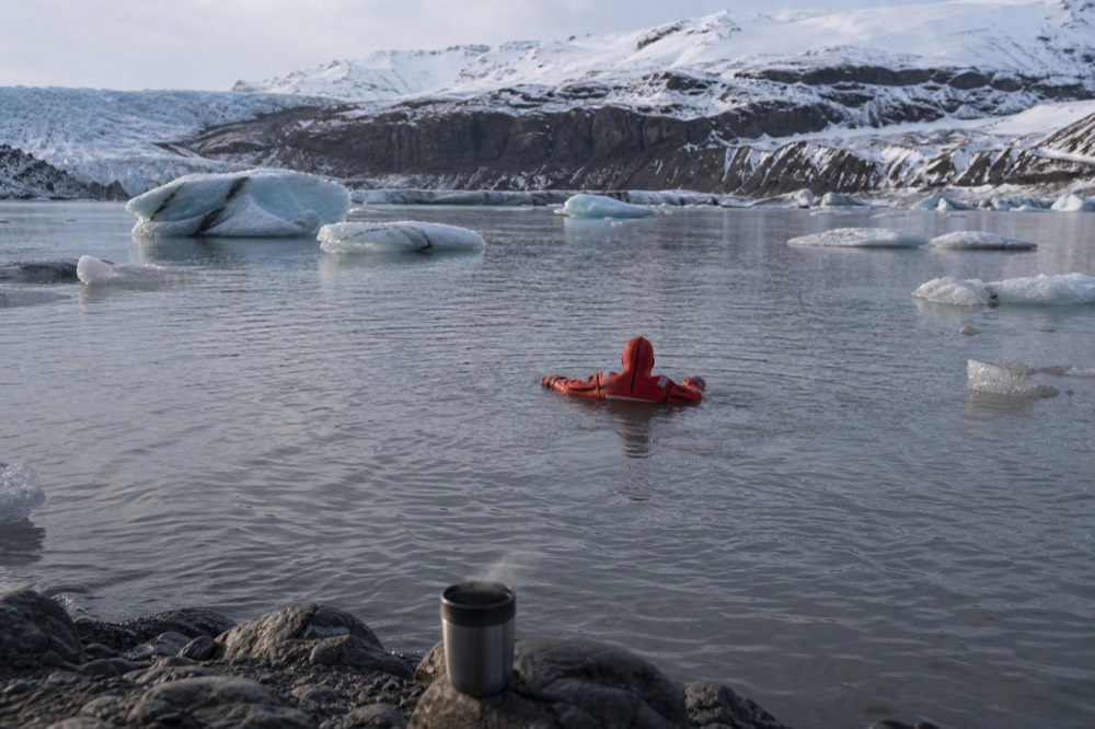 Person in a red thermal immersion suit floating on calm water between small icebergs
