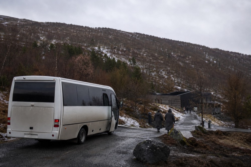A small shuttle bus parked on a gravel road beside a forested hillside