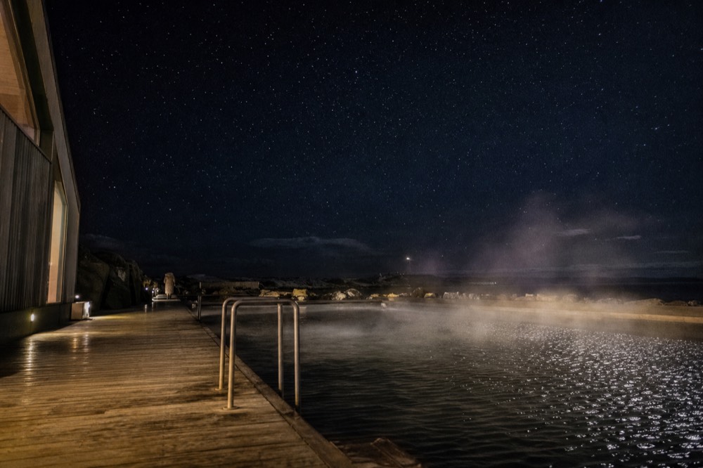 Steam rising from an outdoor pool at night with a starry sky above dark water