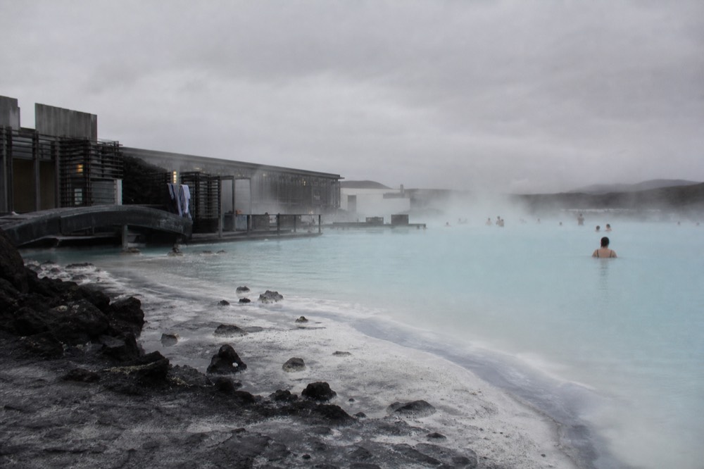 Steam rising from a milky blue geothermal lagoon edged with dark lava rock