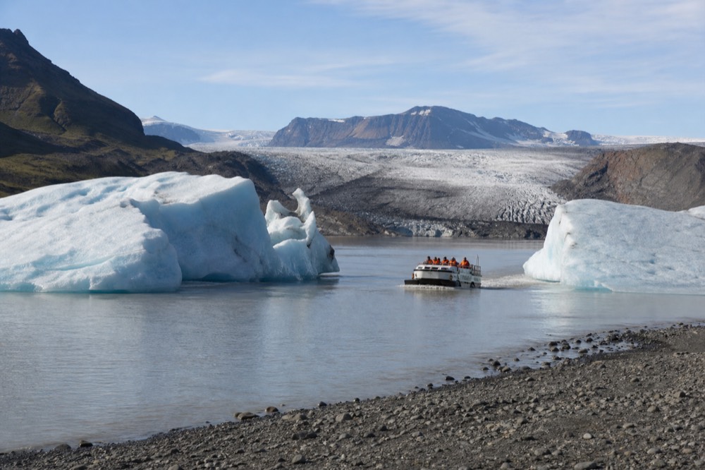A small boat cruising between tall icebergs on a grey glacier lake