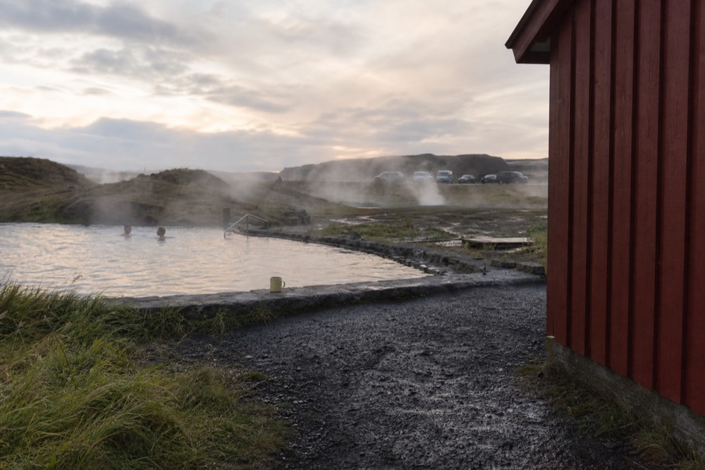 A rustic wooden pool steaming in a geothermal field at dusk