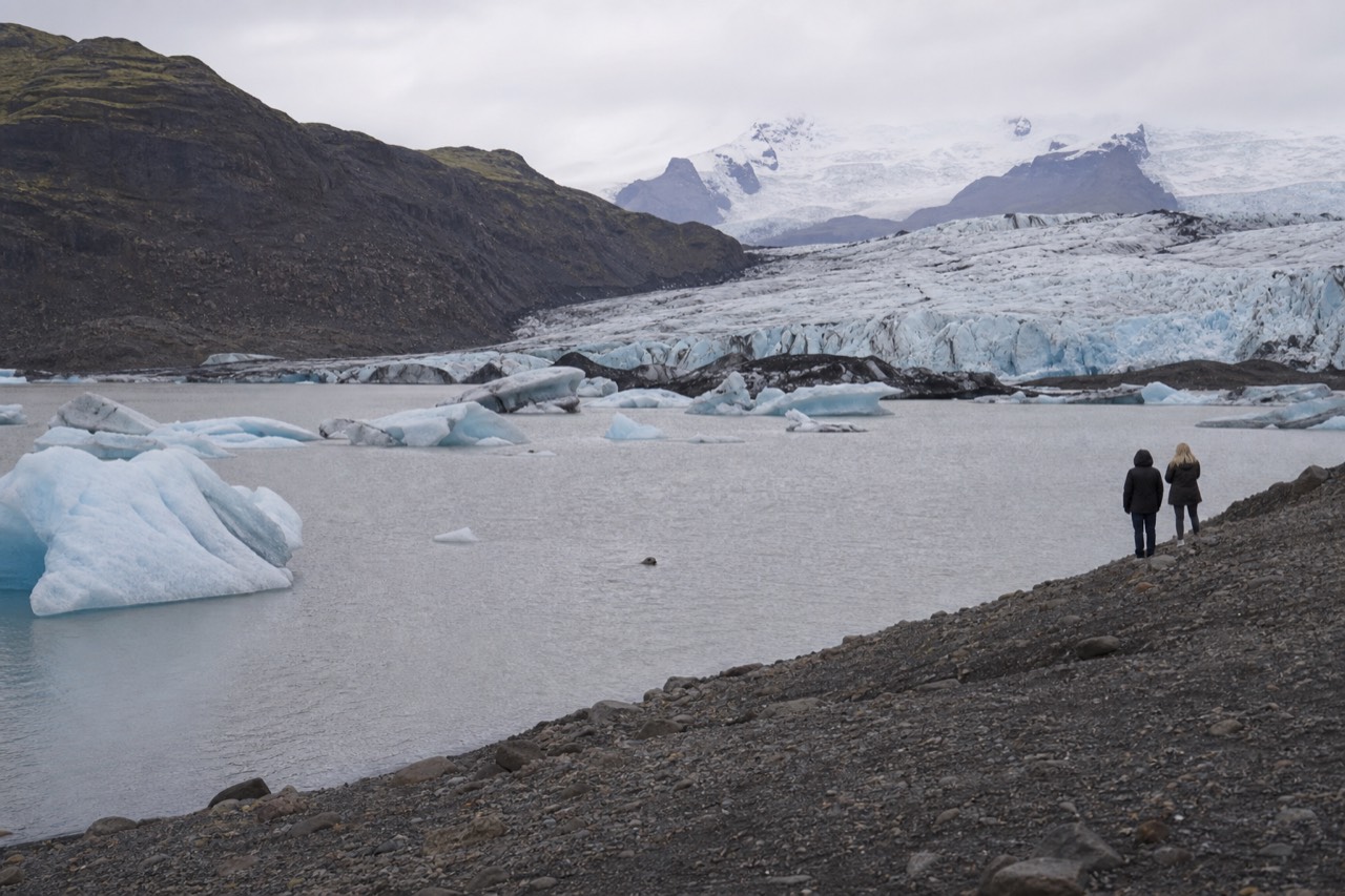 Icebergs floating on a still grey glacier lagoon beneath a low glacier front