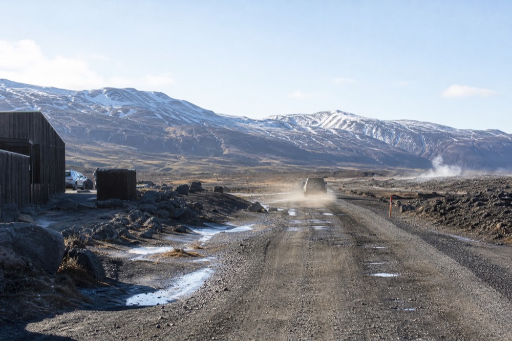 A gravel mountain road crossing a wide highland plain toward distant snow-streaked peaks