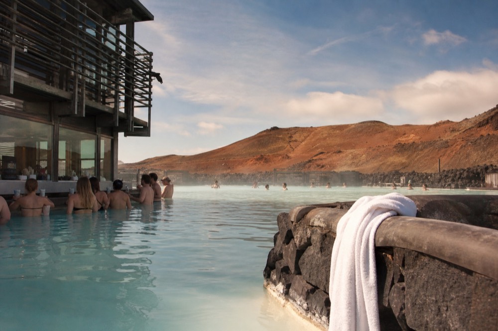 Bathers waist-deep in a steaming pool with a swim-up bar and mountains behind