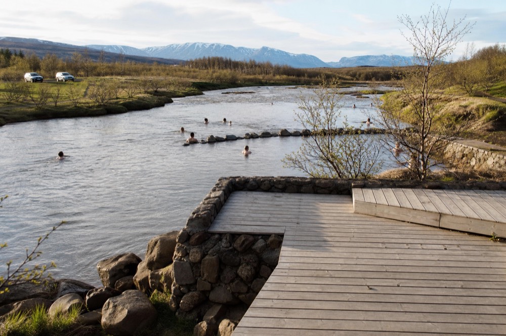A modern geothermal lagoon beside a wide glacial river with green fields around