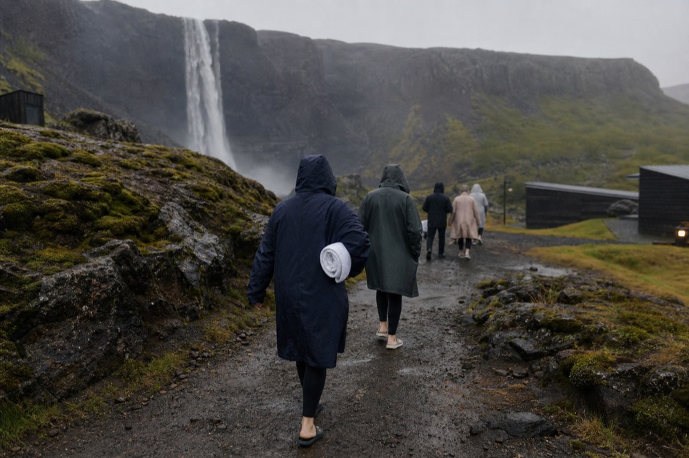 A small group walking a dirt path beside a waterfall on the way to geothermal pools