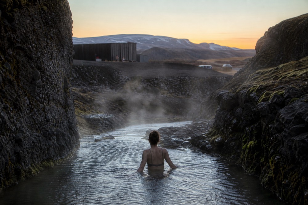 Steam rising from a quiet pool between canyon walls in low evening light